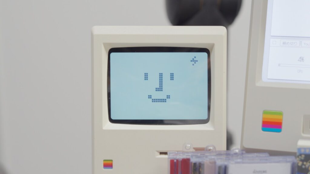初代Macintoshの形をした置き時計Maclockの画面に、ニッコリした顔のマークが出ているところ